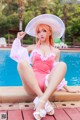 A woman in a pink bathing suit and a white hat sitting by a pool.