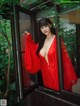 A woman in a red robe is looking out of a window.