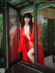 A woman in a red robe is looking out of a window.