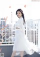 A woman in a white shirt and skirt standing on a balcony.