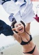 A woman in a black bikini holding up a white shirt.