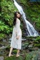 A woman in a white dress standing in front of a waterfall.