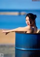 A woman sitting in a blue barrel on the beach.