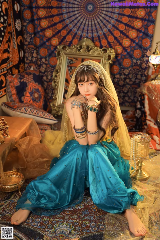 A young girl in a blue dress sitting on a rug.